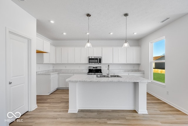 kitchen featuring appliances with stainless steel finishes, pendant lighting, white cabinets, light stone counters, and a center island with sink