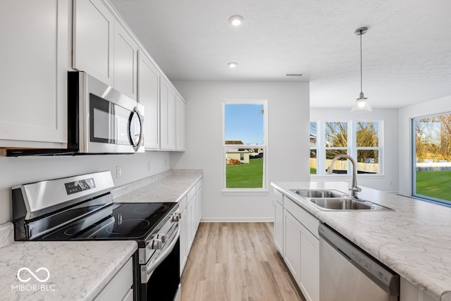 kitchen featuring sink, light wood-type flooring, appliances with stainless steel finishes, pendant lighting, and white cabinets