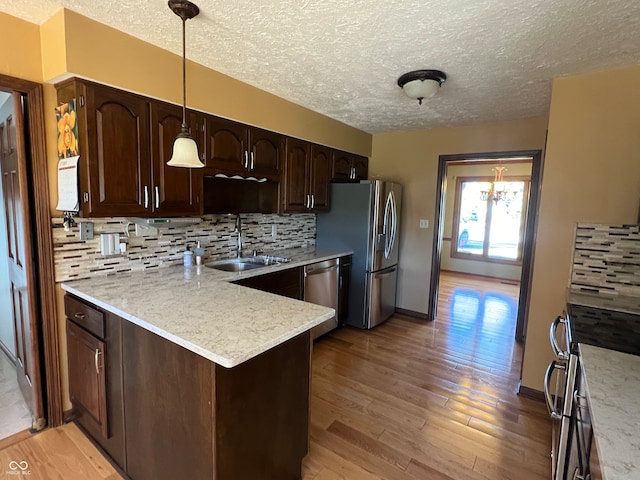 kitchen with hanging light fixtures, sink, kitchen peninsula, appliances with stainless steel finishes, and light wood-type flooring