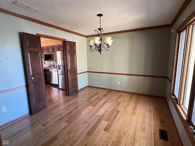 unfurnished dining area with a textured ceiling, wood-type flooring, crown molding, sink, and a chandelier