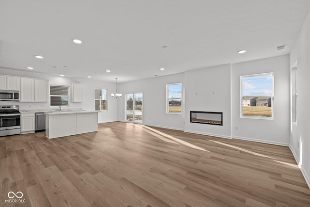 unfurnished living room with sink, a healthy amount of sunlight, a notable chandelier, and light wood-type flooring