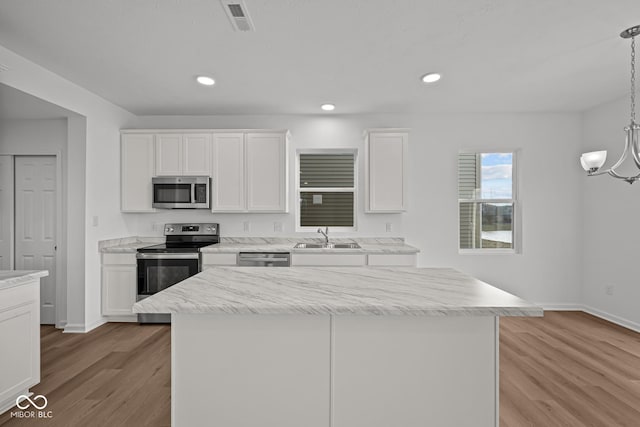 kitchen with white cabinetry, sink, pendant lighting, a kitchen island, and appliances with stainless steel finishes