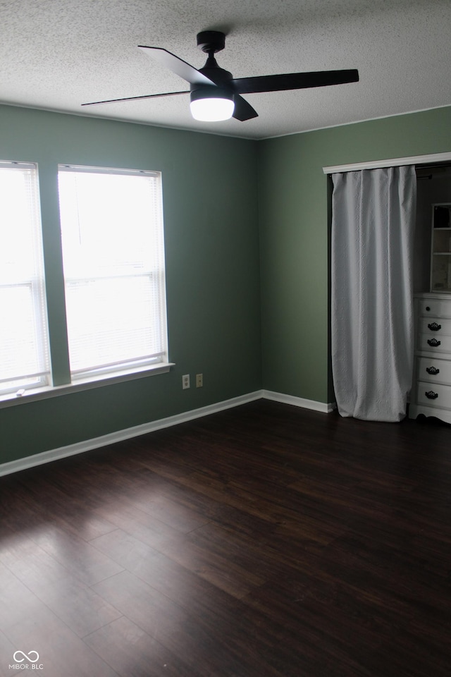 empty room with ceiling fan, dark wood-type flooring, and a textured ceiling