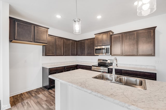 kitchen with light stone countertops, sink, pendant lighting, and appliances with stainless steel finishes