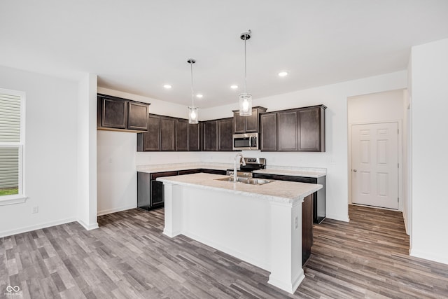 kitchen with pendant lighting, a center island with sink, sink, dark brown cabinets, and light hardwood / wood-style floors