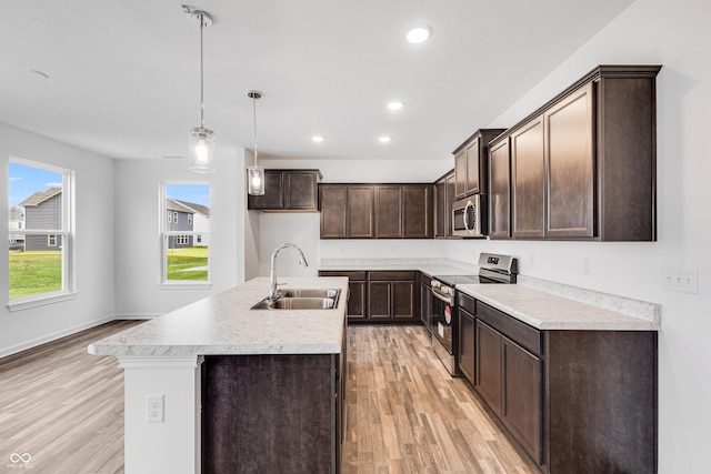 kitchen featuring sink, hanging light fixtures, light hardwood / wood-style floors, a center island with sink, and appliances with stainless steel finishes