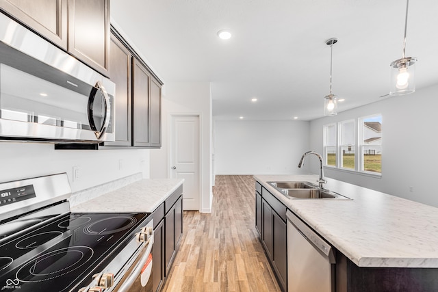 kitchen featuring sink, hanging light fixtures, an island with sink, light hardwood / wood-style floors, and appliances with stainless steel finishes