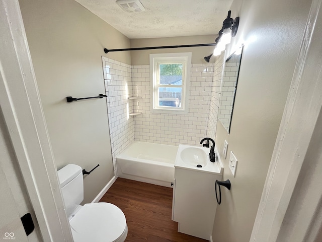 full bathroom with hardwood / wood-style floors, vanity, tiled shower / bath combo, toilet, and a textured ceiling