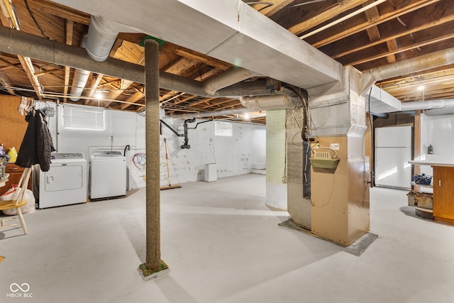 basement featuring washer and clothes dryer, white refrigerator, and heating unit