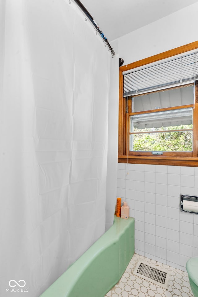 bathroom featuring tile patterned floors, shower / bath combo, toilet, and tile walls