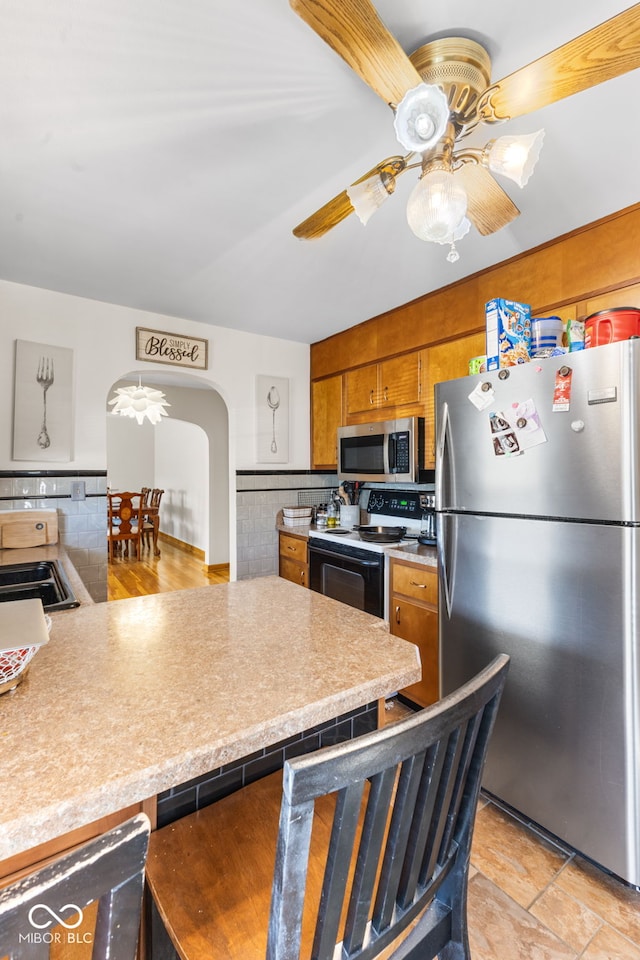 kitchen with ceiling fan, decorative backsplash, stainless steel appliances, sink, and kitchen peninsula