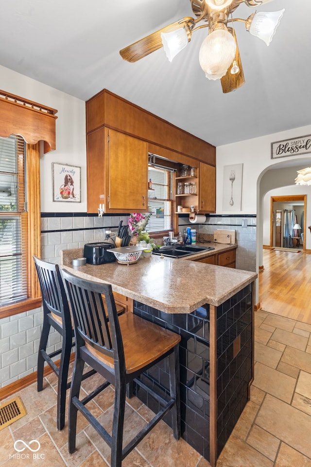 kitchen with light wood-type flooring, ceiling fan, sink, kitchen peninsula, and a kitchen bar