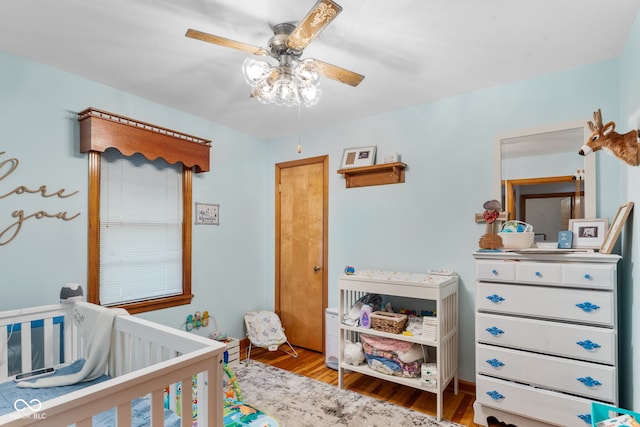 bedroom featuring ceiling fan, a crib, and wood-type flooring