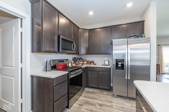 kitchen featuring stainless steel appliances, light hardwood / wood-style floors, dark brown cabinetry, and light stone counters