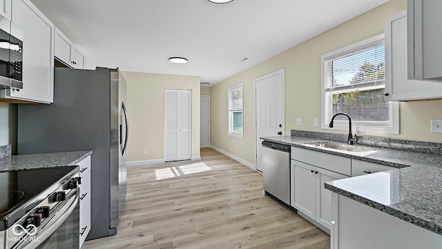 kitchen featuring dark stone countertops, sink, white cabinets, light wood-type flooring, and appliances with stainless steel finishes