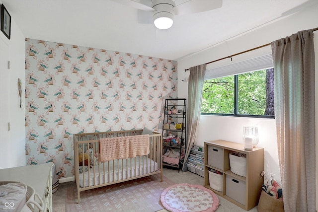 bedroom with a nursery area, light colored carpet, and ceiling fan