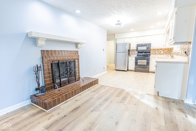 kitchen with a brick fireplace, light hardwood / wood-style flooring, and black appliances