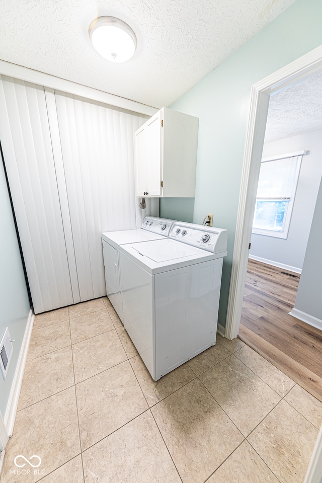 laundry area featuring a textured ceiling, washing machine and clothes dryer, light hardwood / wood-style floors, and cabinets