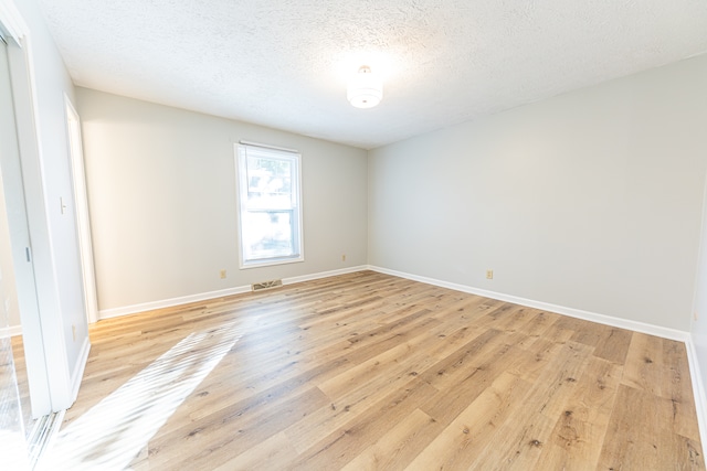 spare room with a textured ceiling and light hardwood / wood-style flooring