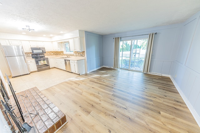 kitchen featuring stainless steel appliances, tasteful backsplash, white cabinets, light hardwood / wood-style flooring, and a textured ceiling