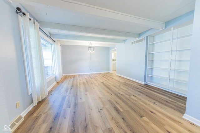 spare room with beam ceiling, a barn door, and hardwood / wood-style floors