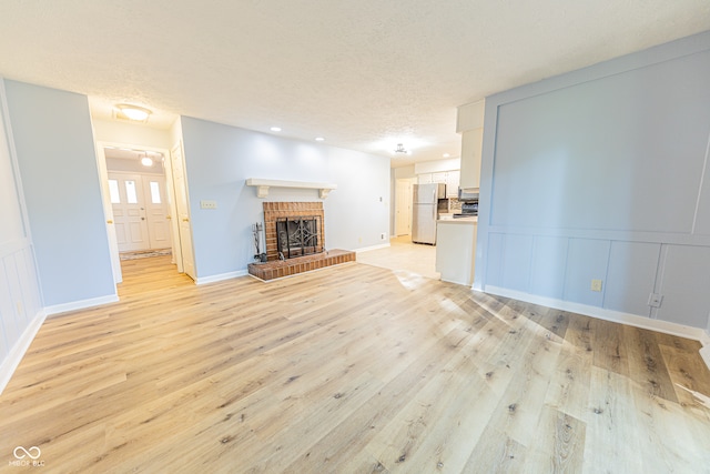 unfurnished living room with a brick fireplace, light hardwood / wood-style floors, and a textured ceiling