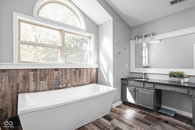 bathroom featuring wood-type flooring, vanity, vaulted ceiling, and a tub