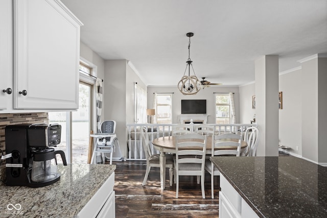 kitchen with decorative light fixtures, white cabinetry, dark hardwood / wood-style floors, dark stone counters, and crown molding