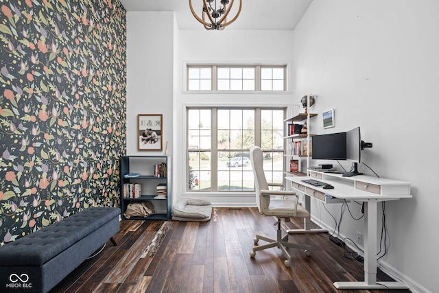 office featuring a notable chandelier, a healthy amount of sunlight, a towering ceiling, and dark hardwood / wood-style flooring