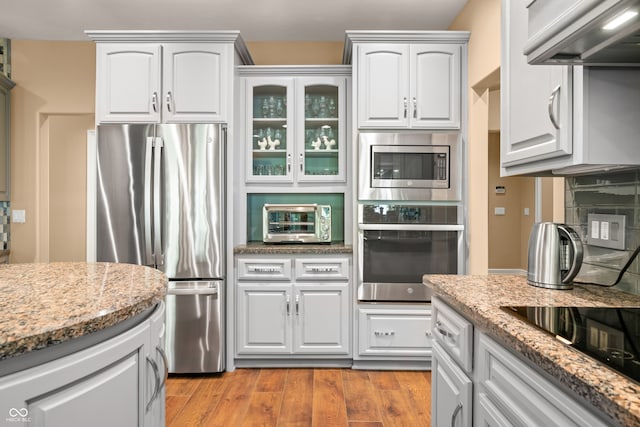 kitchen featuring appliances with stainless steel finishes, white cabinetry, light hardwood / wood-style flooring, light stone counters, and ventilation hood