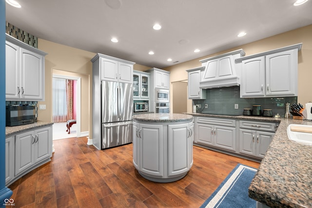 kitchen with tasteful backsplash, a kitchen island, appliances with stainless steel finishes, light stone countertops, and dark hardwood / wood-style floors