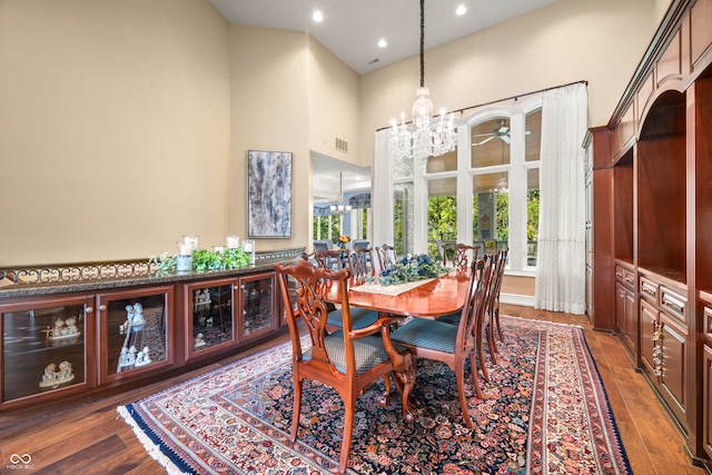 dining room featuring dark wood-type flooring, a high ceiling, and ceiling fan with notable chandelier