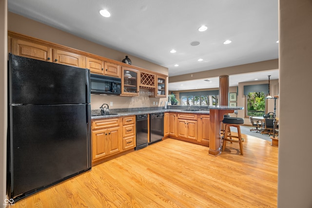 kitchen featuring kitchen peninsula, a breakfast bar area, black appliances, light hardwood / wood-style floors, and decorative light fixtures