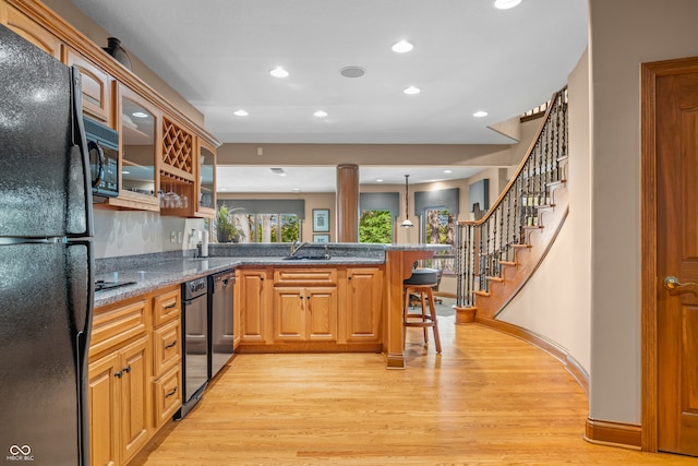 kitchen featuring a kitchen breakfast bar, kitchen peninsula, sink, black appliances, and light wood-type flooring