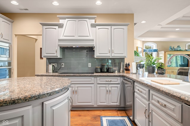 kitchen featuring decorative backsplash, light hardwood / wood-style flooring, sink, light stone countertops, and appliances with stainless steel finishes