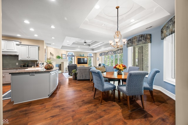 dining room featuring dark wood-type flooring, a raised ceiling, sink, and ceiling fan with notable chandelier