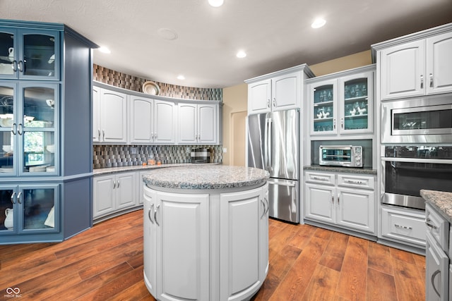 kitchen with appliances with stainless steel finishes, a kitchen island, hardwood / wood-style floors, white cabinets, and decorative backsplash