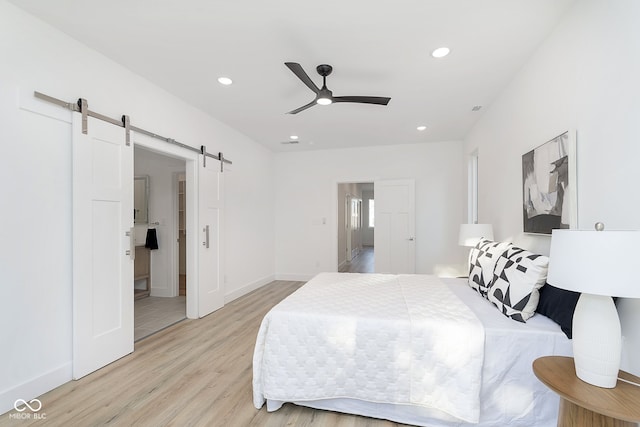 bedroom with a barn door, ceiling fan, ensuite bath, and light wood-type flooring