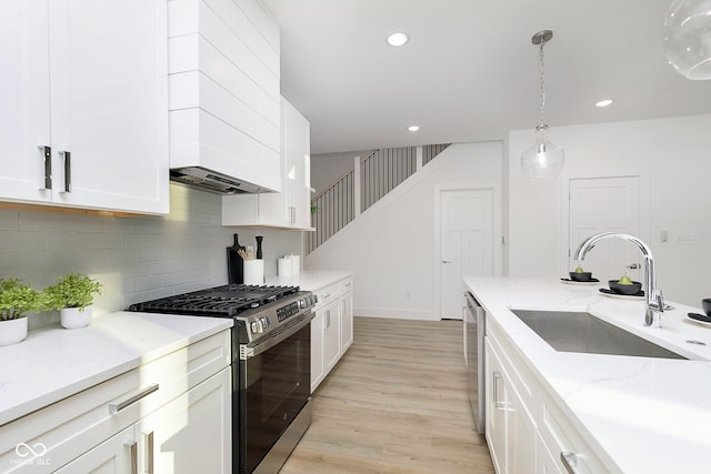 kitchen featuring appliances with stainless steel finishes, light stone counters, sink, decorative light fixtures, and light hardwood / wood-style flooring