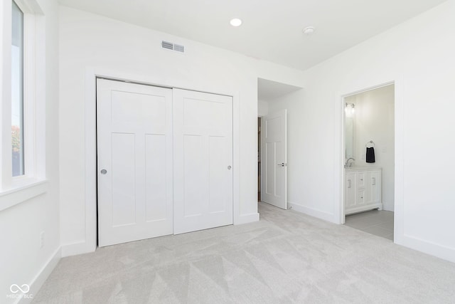 unfurnished bedroom featuring connected bathroom, a closet, and light colored carpet