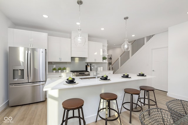 kitchen with appliances with stainless steel finishes, white cabinetry, a kitchen island with sink, and pendant lighting