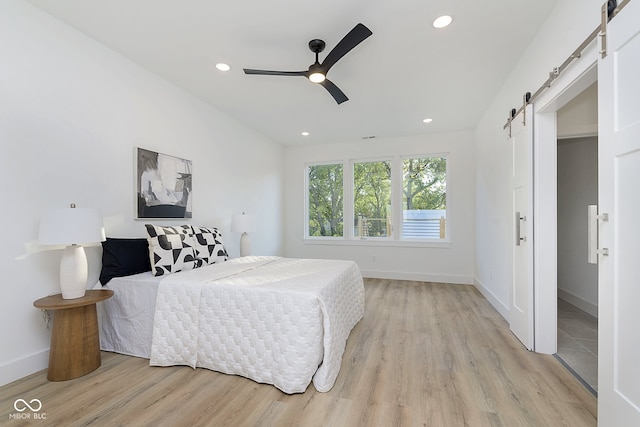 bedroom featuring a barn door, light hardwood / wood-style flooring, and ceiling fan