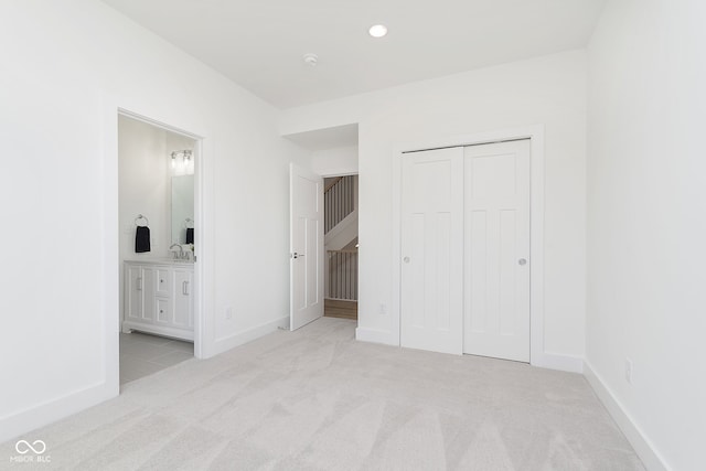 unfurnished bedroom with ensuite bath, light carpet, a closet, and sink