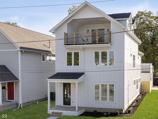 view of front facade with central AC unit, a balcony, and a front lawn