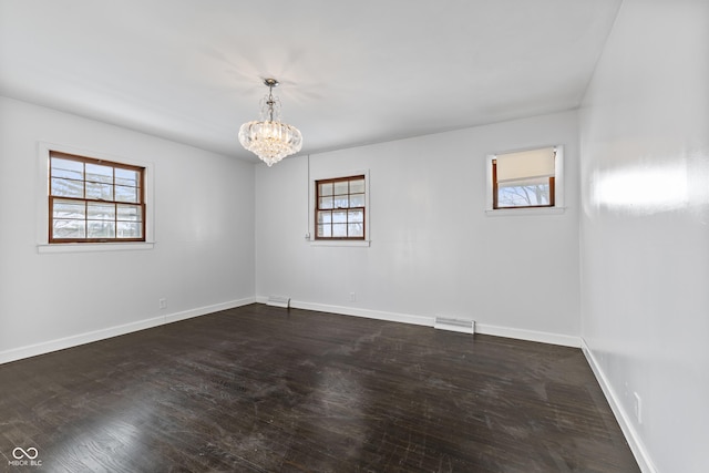 spare room featuring a chandelier and dark wood-type flooring