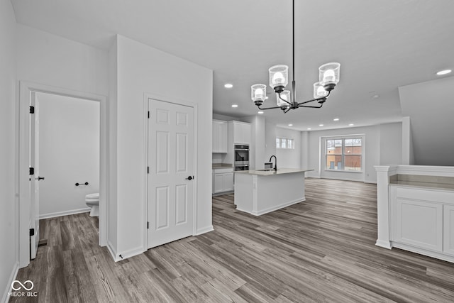 kitchen featuring light wood-type flooring, sink, decorative light fixtures, white cabinetry, and an island with sink