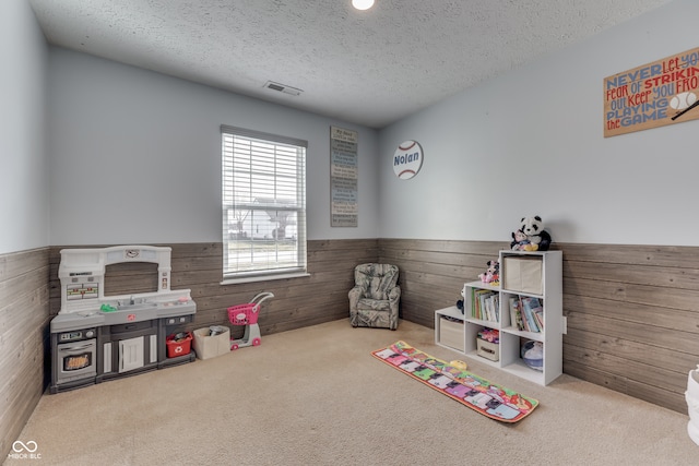 game room featuring a textured ceiling, wood walls, and carpet flooring