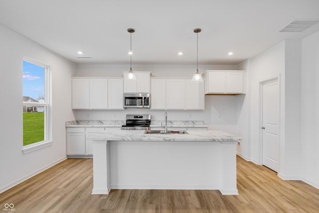 kitchen with white cabinetry, light stone countertops, decorative light fixtures, a center island with sink, and appliances with stainless steel finishes