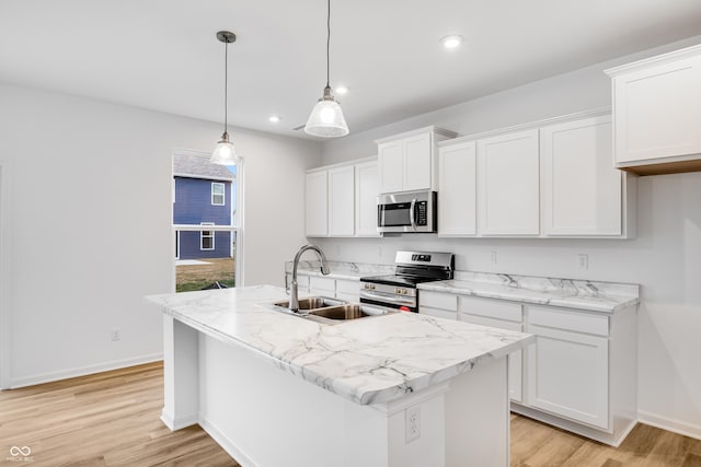 kitchen with a kitchen island with sink, white cabinets, stainless steel appliances, and decorative light fixtures