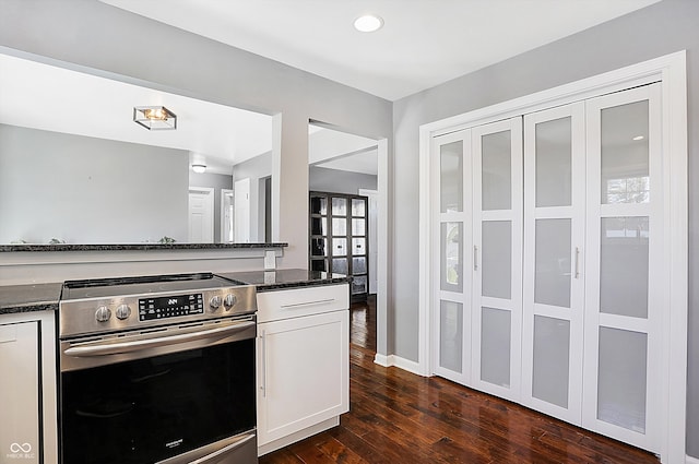 kitchen featuring dark wood-type flooring, dark stone counters, stainless steel stove, and white cabinets